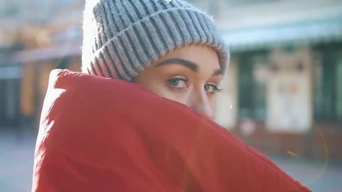 Winter Scene with Woman Wearing Red Blanket and Grey Beanie Looking Over Her Shoulder in Urban Area