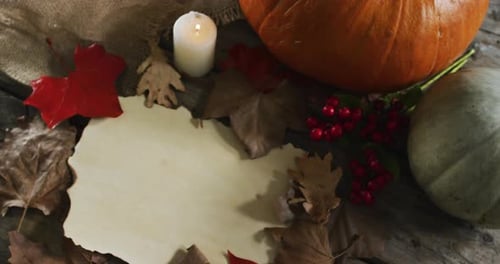 Paper with copy space against autumn leaves, candle and pumpkins on wooden surface
