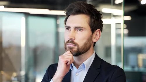 Businessman indoors with thoughtful expression, contemplating ideas in modern office. Man looking