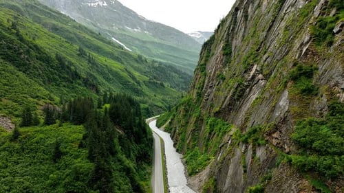 Drone footage along the steep cliff rock with a river at the foot. A highway goes along the river.