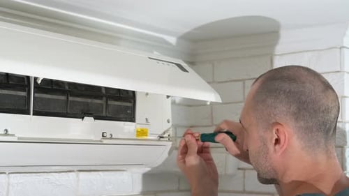 Man Repairing Air Conditioner with Screwdriver Indoors