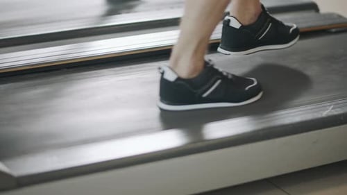 Closeup Feet Running Back on Treadmill in Fitness Gym. Black Sneakers Jumping