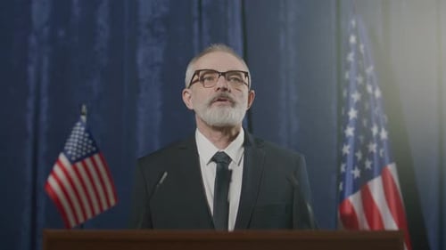 Man in Suit Speaking at Podium with Flags