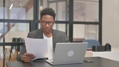 Young Adult Reviews Paperwork at Office Desk
