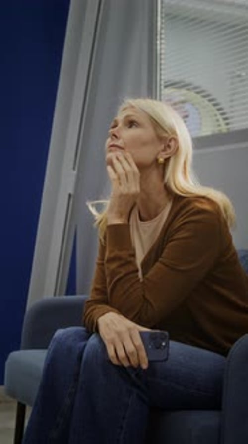 Nervous Woman Sits on Couch in Hospital Corridor Looking at Phone