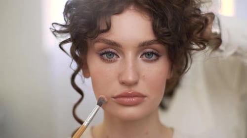 Closeup Portrait of Young Sensual Woman Looking at Camera During Professional Makeup in Modern