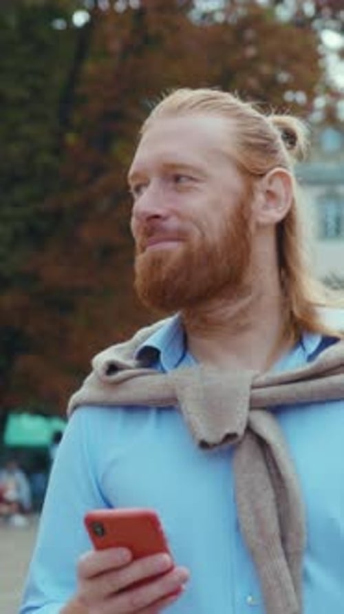 A Casual Man Joyfully Using a Smartphone While Enjoying the Outdoors in a Park Setting