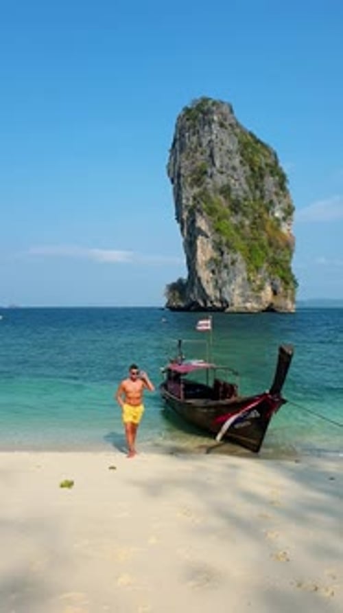 Young Men Walking on the Beach of Koh Poda Krabi Thailand with a Longtail Boat at the White Beach