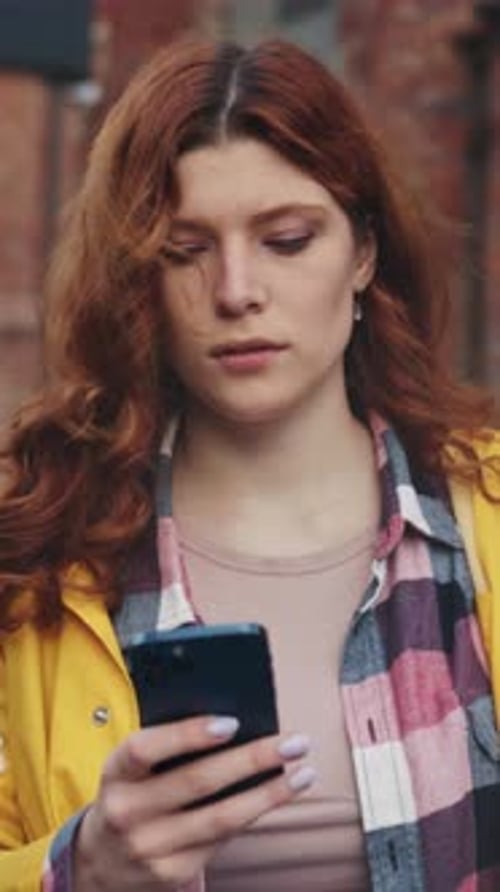 Gingerhaired Woman Walking Fieryhaired Female Dressed Casually Strolling and Checking Her Mobile