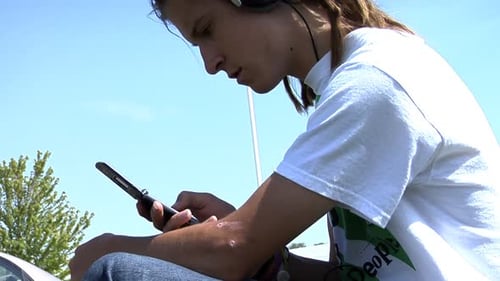 Young man outside using flip phone and headphones