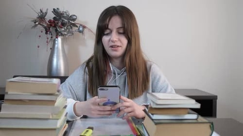 Young Woman Using Phone with Books at Desk