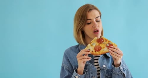 Young Woman Enjoying Slice of Pizza on Blue Background