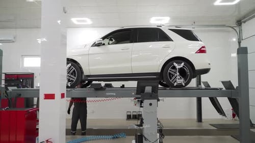Auto Technician Aligns Wheels on Lift in Modern Garage Vehicle Servicing for Optimal Performance in