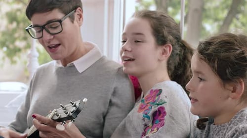 Woman and girls singing along to a ukulele