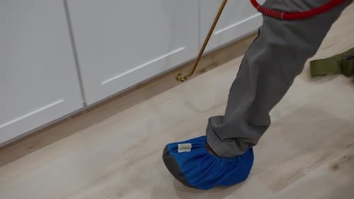 Anwendung der Pestizidbehandlung mit einem Sprühschlauch entlang der inneren Fußleisten von Küchenschränken für