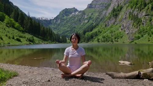 Pretty woman practice yoga exercise on shore of lake between green mountains. Sunny summer day in Sw