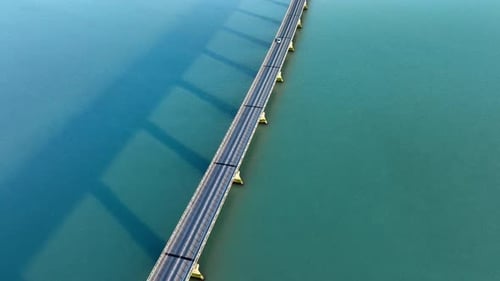 Symmetrische Linien und Schatten auf einer Ozeanbrücke über türkisfarbenem Wasser, Drohnenaufnahme eines Autos
