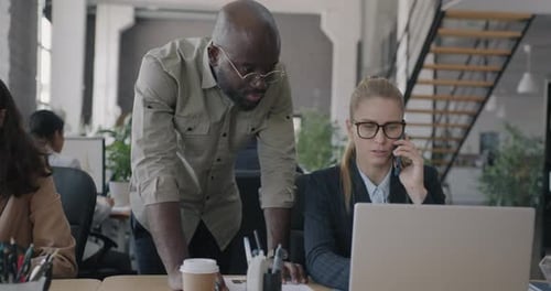 Young Businesswoman Speaking on Mobile Phone Talking to Colleague and Pointing at Laptop Screen in