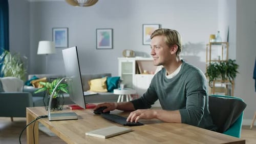 Porträt des konzentrierten jungen Mannes, der an einem PC arbeitet, während er an seinem Schreibtisch sitzt. In der