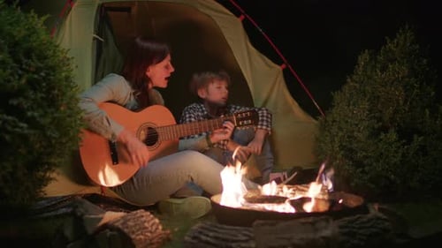 Woman and Child Playing Guitars Near Tent at Night