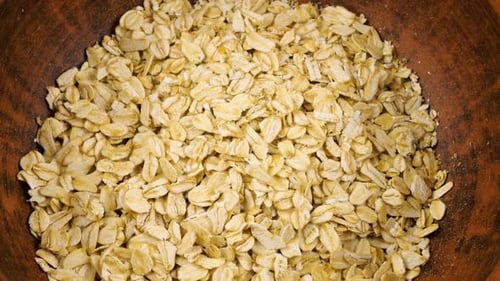 Oatmeal is poured into a terracotta clay bowl against a wooden board. Top view.