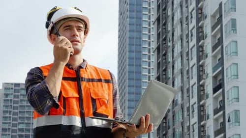 Young man engineer checking information from laptop and talking on radio call with colleague