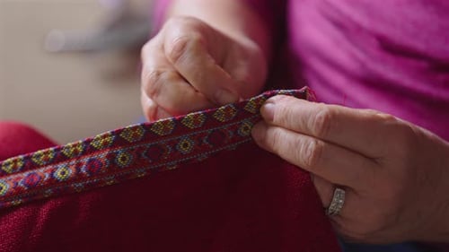 Ältere Hände nähen farbenfrohe, folkloristische Verzierungen auf roten Stoff
