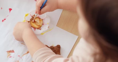 Child Paints a Small Object at a Table