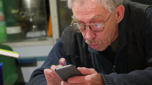 An aged man curiously scrolls the phone display with his fingers.