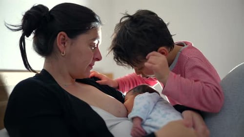 Mother Nursing Newborn with Child Watching Indoors