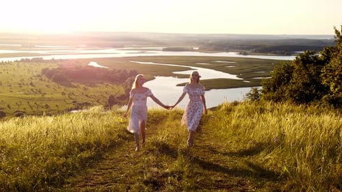 Two Blonde Girlfriends in Identical Dresses Hold Hands and Walk Up the Hill