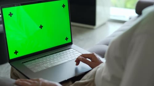 Woman sitting in living room working on laptop with Green Mock Up Screen