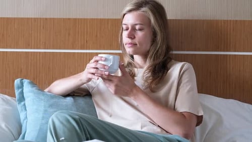 woman sitting on bed in hotel room drinking coffee in the morning