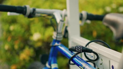 Close up of a cable lock securing a blue bike to a white fence