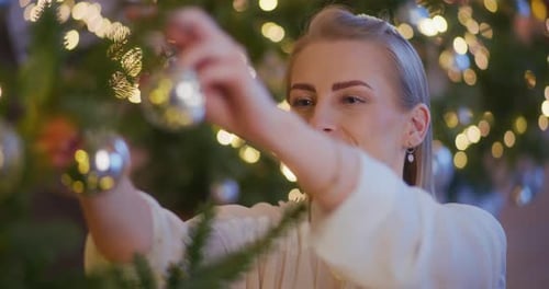 Woman Decorates Christmas Tree with Silver Ornaments