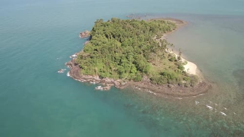 Aerial ascending shot looking down on tropical island beach, jungle and rocky coastline