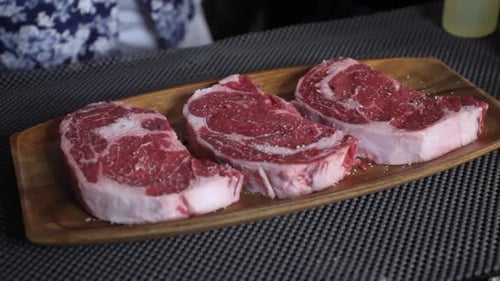 Close up shot of chef strewing salt and pepper at fresh raw beef steak on wooden board.