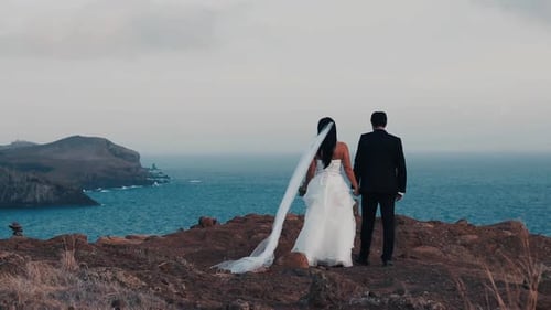 Newly weds married couple slowly walking towards ridge cliff wedding day romantic sunset oceanveiw p