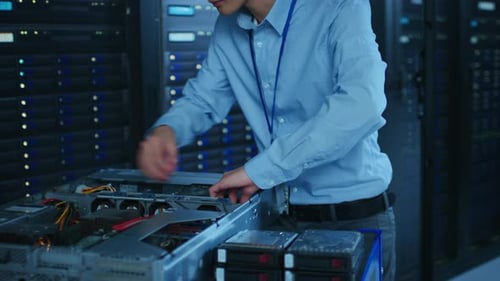 In the Modern Data Center: IT Technician Wearing Protective Headphones Working with Server Racks, o