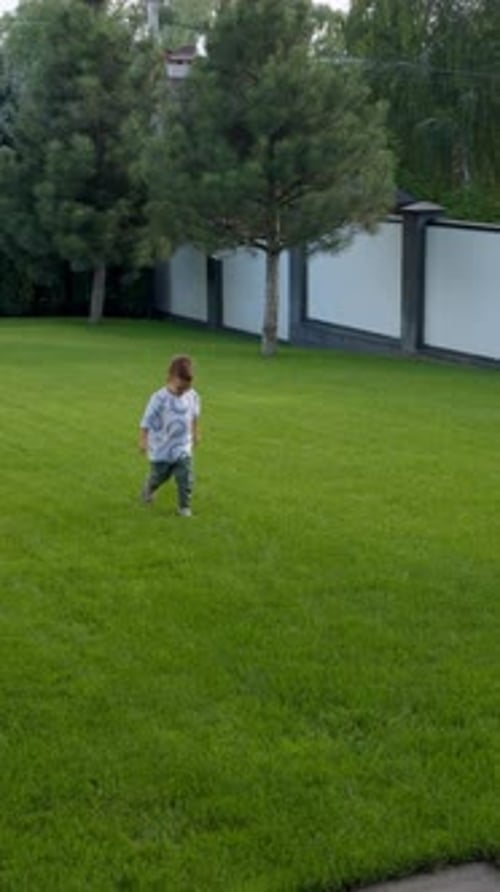 Cheerful energetic Caucasian baby boy runs by the green lawn.