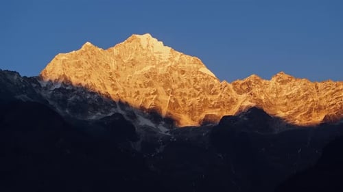 Mountain Peak Glowing Under Sunrise Golden Rays Highlighting Snowy Everest Summit with Steep Rocky