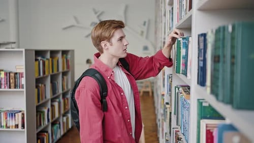 Freshman Student Takes Book with Green Cover From Rack Shelf