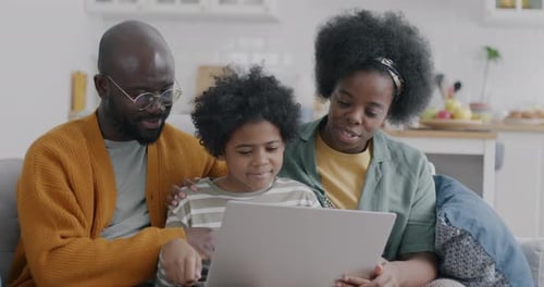 Little African American Boy Using Laptop Computer with Father and Mother Sitting on Couch at Home