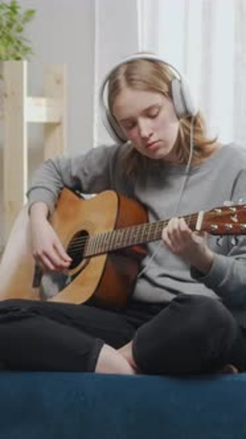 Young Musician Practicing Acoustic Guitar Chords with White Headphones Sitting Crosslegged Indoors