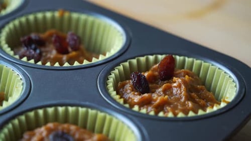 Adding raisins to batter inside of pan for vegan pumpkin muffins using real roasted pumpkin in bowl