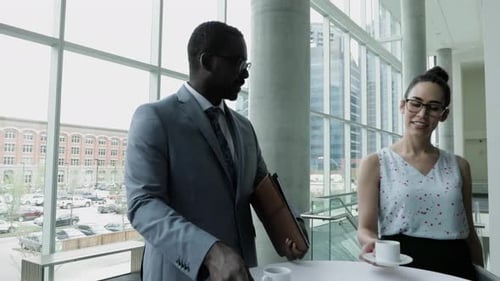 Businessman and Businesswoman with Coffee Talking at Table in Office African American Ethnicity