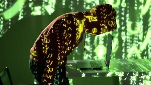 Hacker in Hoodie Leaning Over Laptop with Green Digital Code Projections – 4K Cybersecurity Visual