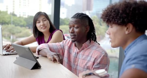 Discussing project, diverse colleagues collaborating using tablet and laptop in office