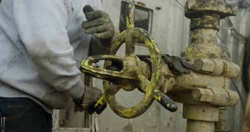 Unrecognized worker wearing dirty gloves rotates the large faucet on the oil pipe.