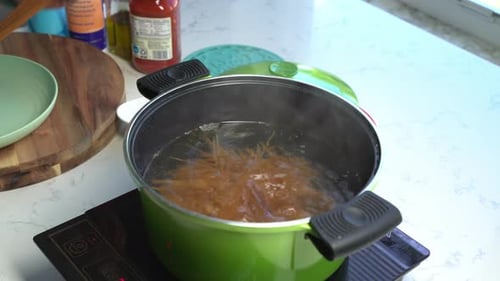 Cooking spaghetti at home, close up view of breaking pasta into a boiling pot of water